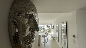 Un intérieur moderne agrémenté d’une grande œuvre d’art métallique murale, d’un coin repas offrant une vue sur la mer et d’œuvres d’art encadrées qui décorent les murs.