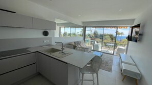Une cuisine moderne dotée d’un îlot central, un coin repas offrant une vue sur l’océan et un balcon avec un espace salon extérieur.