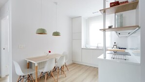 A modern kitchen with white cabinetry, a wooden dining table, and two pendant lights. - Nice and cozy apartment in Pamplona center! (Pamplona/Iruña)