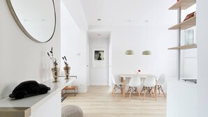 A modern, minimalist interior with a dining area featuring a round table and white chairs, a small seating area with a round ottoman, and a wall-mounted mirror. - Nice and cozy apartment in Pamplona center! (Pamplona/Iruña)