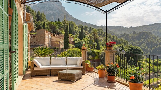 A terrace with a wicker sofa and ottoman, potted plants, and a view of a mountainous landscape. - SA VOLTA DE CA NóLIVER DEIA Villa with New Pool & Sea and Mountain Views (DEIA)