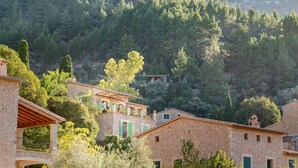 A stone building with a balcony, surrounded by lush greenery and a mountainous backdrop. - SA VOLTA DE CA NóLIVER DEIA Villa with New Pool & Sea and Mountain Views (DEIA)