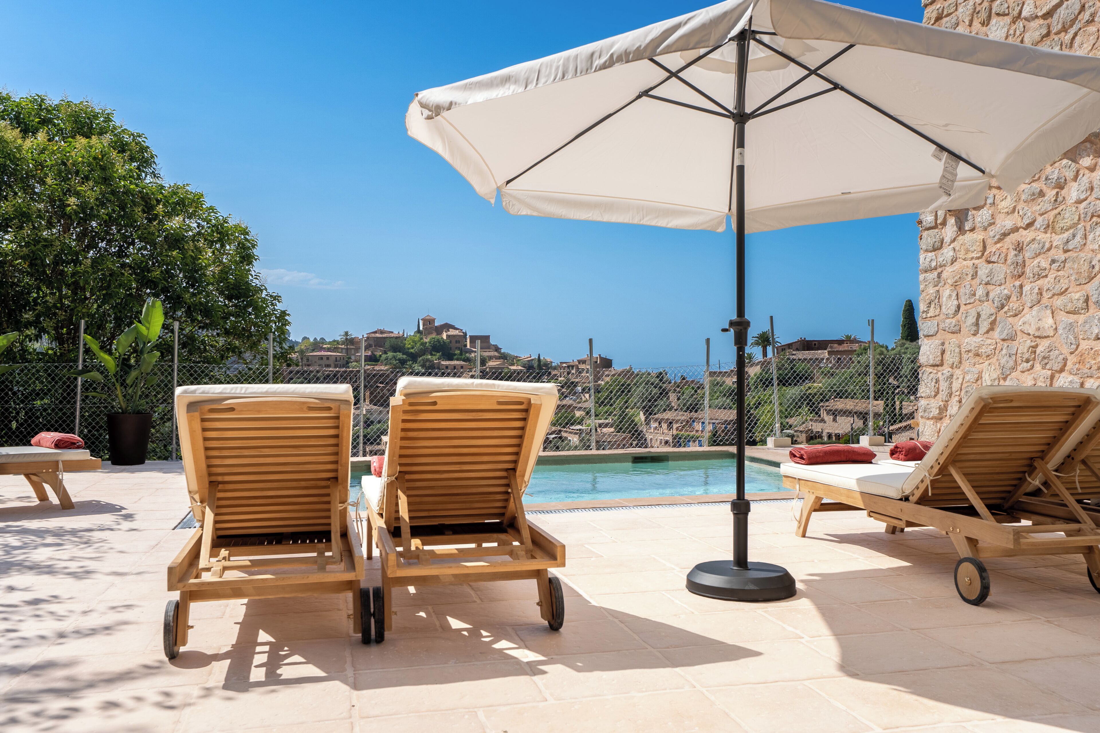 A poolside area with lounge chairs and an umbrella, overlooking a scenic view of a town.