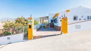 A building with a white facade, a yellow entrance gate, and a staircase leading to a covered area with a view of the mountains.