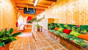A wooden interior with a tiled floor, a sofa with tropical prints, and a television mounted on the wall.