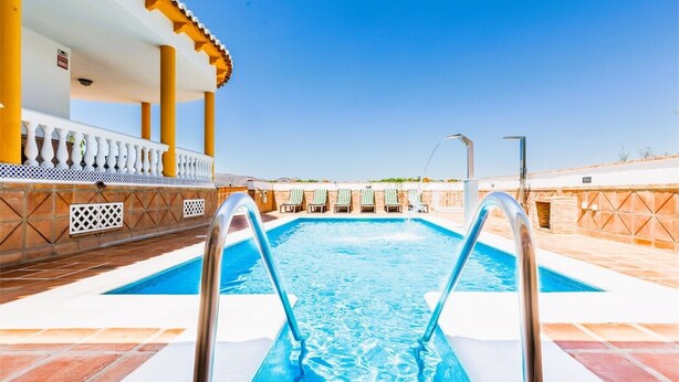 A swimming pool with a clear blue water, surrounded by a tiled deck and a white balustrade.