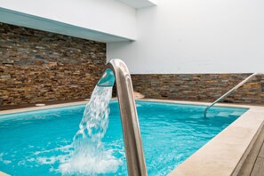 A swimming pool with a water feature, a metal ladder, and a stone wall in the background.