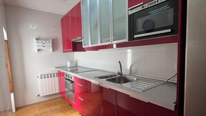 A kitchen with red cabinets, a stainless steel sink, and a built-in oven. - The Feng Shui House Perseverance for 4 people (Aldehuela)