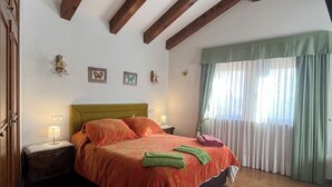 A bedroom with a wooden ceiling, a bed with a green and orange bedspread, two bedside lamps, and a window with curtains. - The Feng Shui House Perseverance for 4 people (Aldehuela)