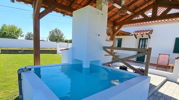 Una piscina con una estructura blanca en el centro, rodeada por un patio cubierto con suelo de baldosas.