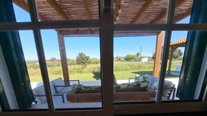 Habitación con vistas a una zona verde, una pérgola de madera y un espacio de descanso con cojines.