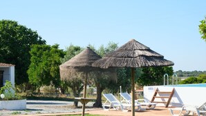 Un área de piscina con sillas de descanso, una sombrilla de paja y una terraza de madera.