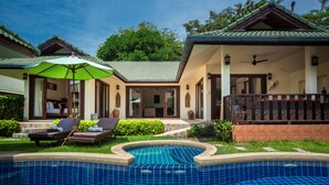 A pool area with lounge chairs and umbrellas, a covered patio, and a building with a tiled roof. - Deluxe 3 bed room pool villa in beach resort Idyllic Samui (Ko Samui)