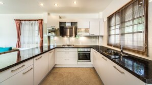 Een moderne keuken met witte kasten, een zwart aanrecht, roestvrijstalen apparatuur en een raam met jaloezieën.