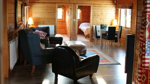 A log cabin interior with a loft bedroom, a dining area, and a living room with a sofa and chairs.