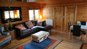 A cozy cabin-style room with a brown leather sofa, a matching ottoman, and a dining table with chairs.