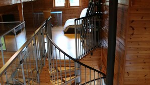 A cabin with a wooden interior, a staircase, a fireplace, and a window.