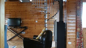 A wooden interior with a staircase, a fireplace, a television, and a sofa.