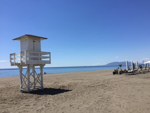Ein Rettungsschwimmturm an einem sandigen Strand mit freiem Blick auf den Ozean und ferne Berge.