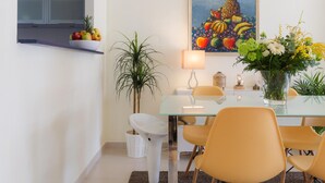 A dining area with a glass table, yellow chairs, a white lamp, and a painting of fruits on the wall. - Beautiful apartment near the beach (Rincón de la Victoria)