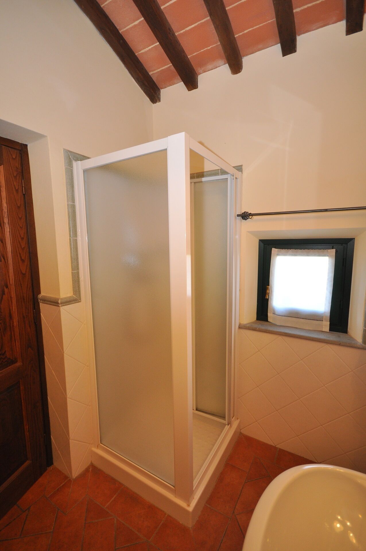 A bathroom with a glass-enclosed shower, a window with a curtain, and a bathtub.
