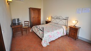 Un dormitorio con cama, dos mesitas de noche con lámparas, un armario de madera, una silla y un escritorio con televisor.