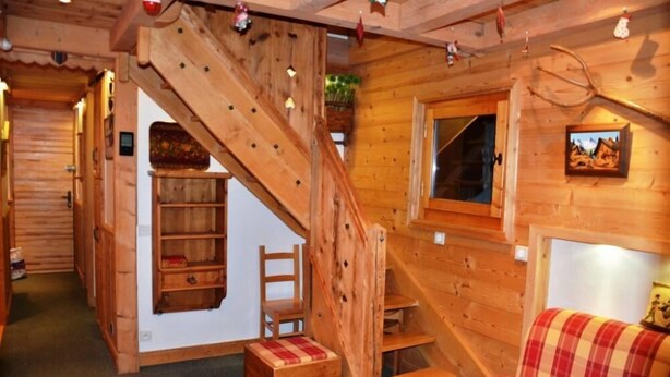 A cozy cabin interior with a wooden staircase, a sofa, and a window with a picture.