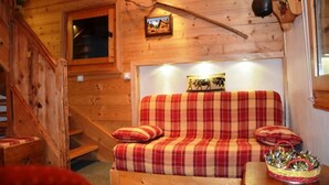 A wooden cabin interior with a plaid sofa, a small window, and a staircase.