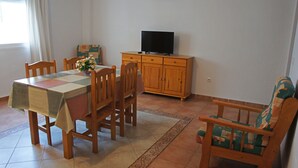 A dining area with a table, chairs, a television on a cabinet, and a window with curtains. - Comfortable apartment within walking distance of Almería (Alhama de Almería)
