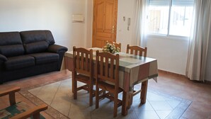 A living room with a dark blue sofa, wooden dining table with four chairs, and a tiled floor. - Comfortable apartment within walking distance of Almería (Alhama de Almería)