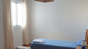 A room with two beds, a window with curtains, a wooden nightstand with a lamp, and a hanging light fixture. - Comfortable apartment within walking distance of Almería (Alhama de Almería)