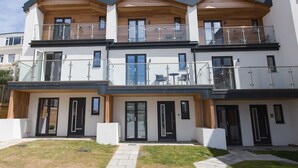 Un edificio residencial moderno de varios pisos con balcones, ventanas amplias y un césped cuidado.