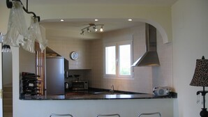 Una cocina moderna con una isla central, taburetes de bar, un refrigerador, un microondas y un reloj en la pared.