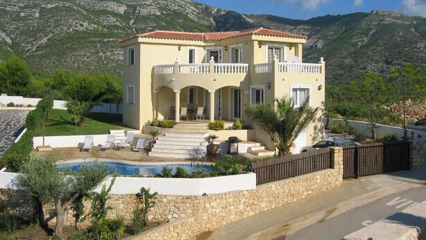 Una villa de estilo mediterráneo de dos pisos con piscina, mobiliario exterior y vistas a las colinas circundantes.