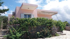 A modern house with a pink facade, a stone wall with climbing plants, and a stone staircase leading to the entrance. - Bay View Villa I in Crete with private swimming pool and modern convenient (Chania)