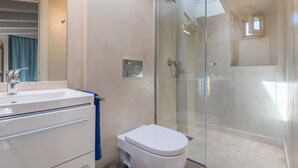 A modern bathroom with a glass shower enclosure, a white toilet, and a vanity with a mirror. - Sa Caseta. (Sóller)