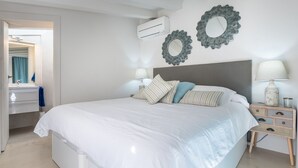 A bedroom with a large bed, two wall mirrors, a bedside table with a lamp, and an air conditioning unit. - Sa Caseta. (Sóller)