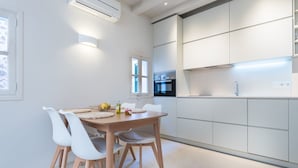 A modern kitchen with white cabinetry, a built-in oven, and a dining area with a wooden table and white chairs. - Sa Caseta. (Sóller)