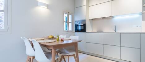 Ett modernt kök med vita skåp, en inbyggd ugn och en matplats med ett träbord och vita stolar.