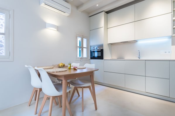 A modern kitchen with white cabinetry, a built-in oven, and a dining area with a wooden table and white chairs.