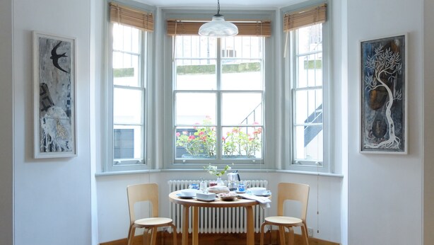 Ruokailutilassa on pyöreä pöytä, neljä tuolia ja taideteoksia seinillä.