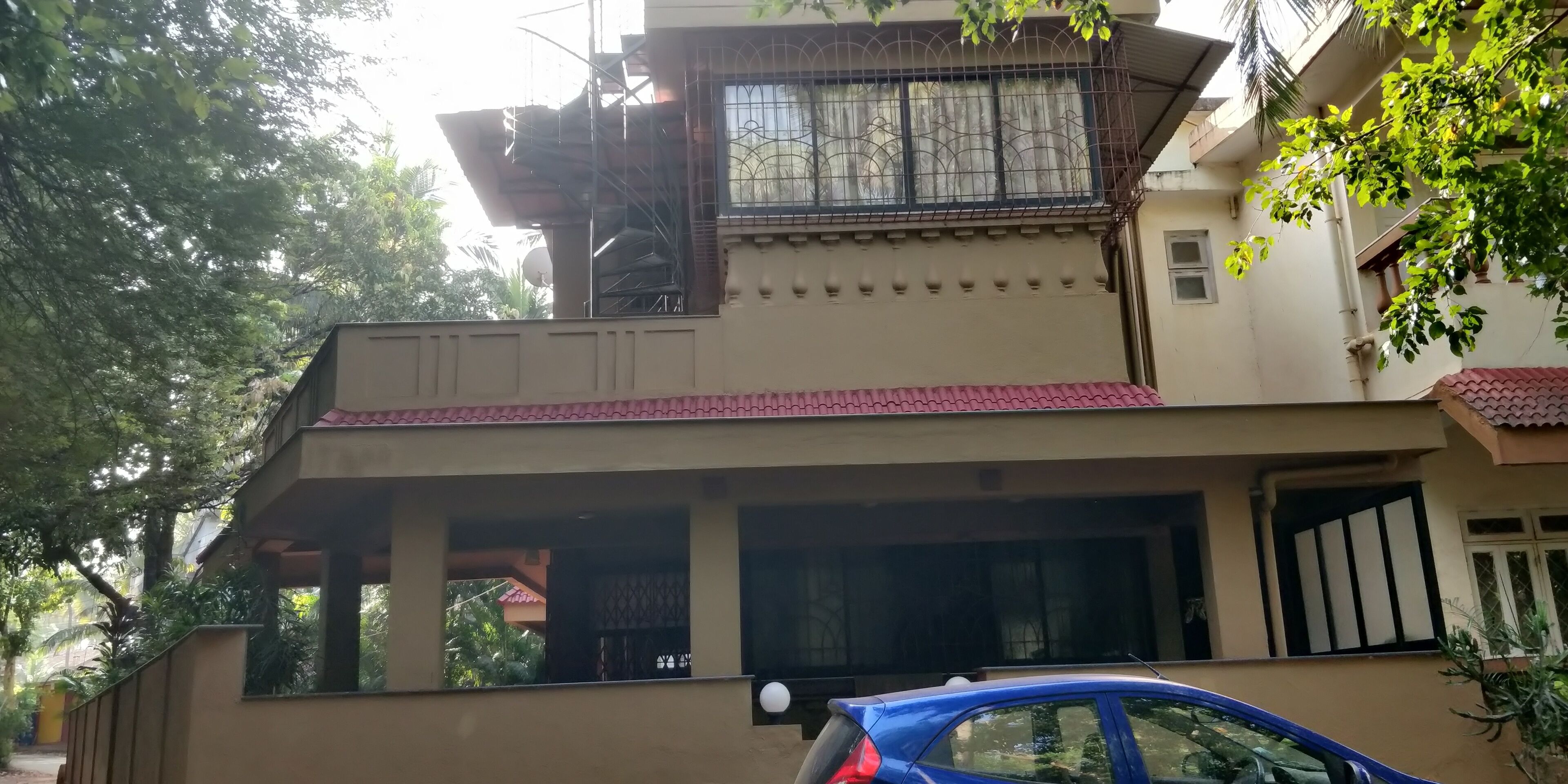 Um edifício residencial com telhado de telhas vermelhas, uma varanda com grades de metal e uma porta de garagem.