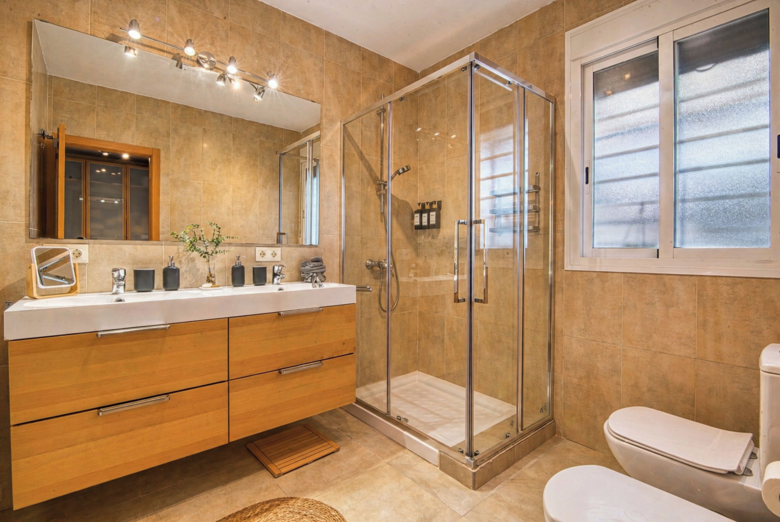 Une salle de bain moderne avec une douche à parois de verre, un grand miroir et des toilettes blanches.