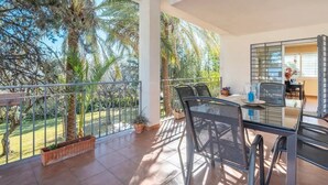 Un balcó amb taula i cadires de vidre, amb vista a un jardí de palmeres i al cel.