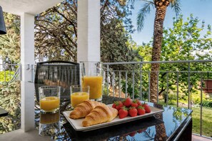 A breakfast setup with croissants, strawberries, and orange juice on a balcony with a view of trees and a clear sky. - VillaSense Luxury | Golf, Pool & Nature | Seville (Guillena)