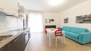 Eine moderne Küche mit weißen Schränken, einem Esstisch mit roten Stühlen und einem türkisblauen Sofa in einem hellen Wohnbereich.