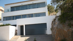 Une maison moderne à deux étages, dotée d’un grand portail de garage, d’un mur de soutènement en pierre et d’un escalier menant à l’entrée.
