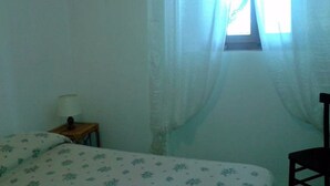 Una stanza piccola e arredata in modo essenziale, con un letto singolo, un comodino e una sedia.