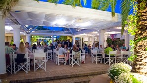 An outdoor dining area with white tables and chairs, covered by a white canopy, surrounded by greenery and flowers. - Bouganville Residence - Elite apartment with swimming pool, sports field and games. (Calatabiano)