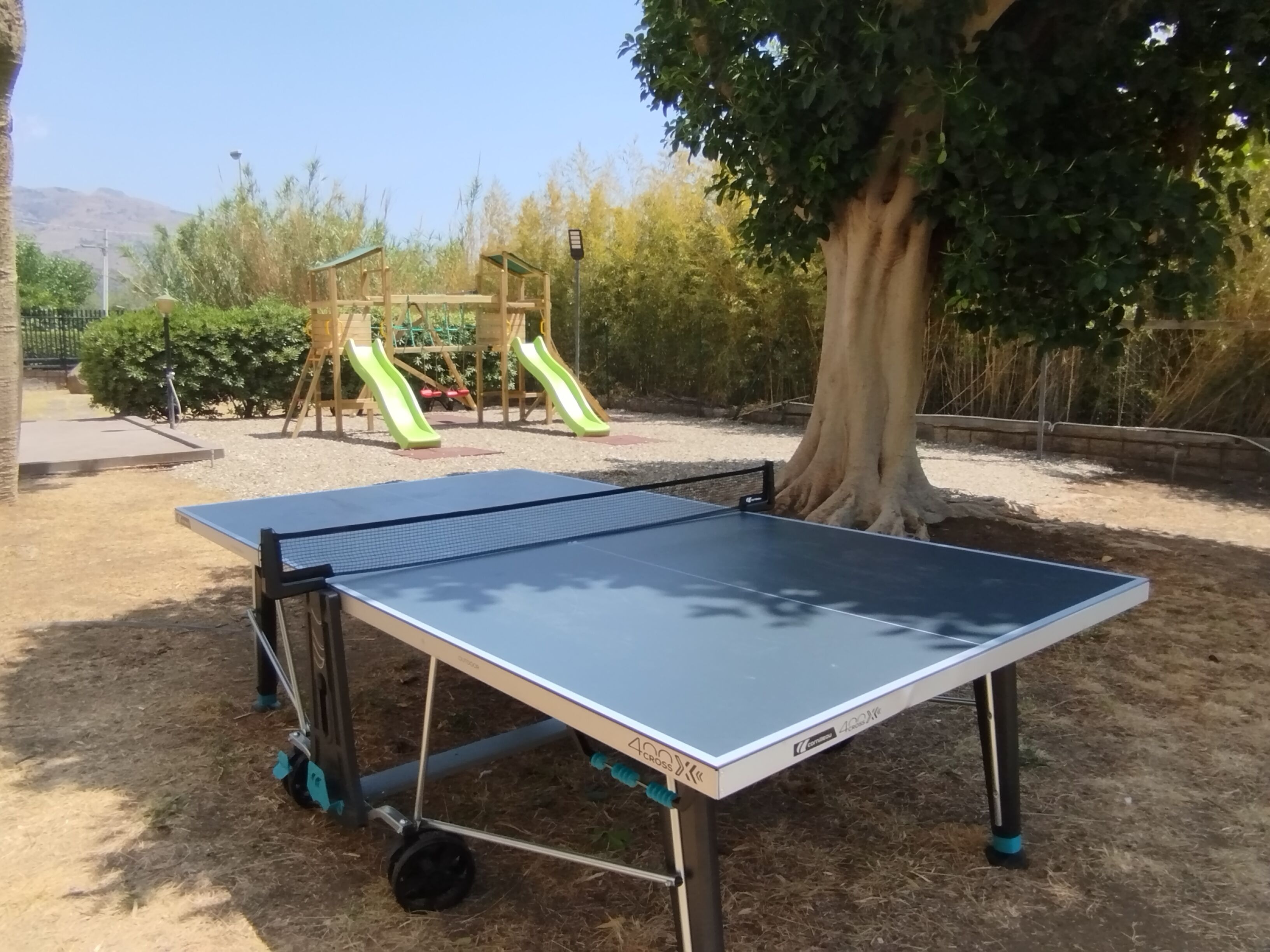 Ein Tischtennistisch in einem Außenbereich mit einem Spielplatz im Hintergrund.